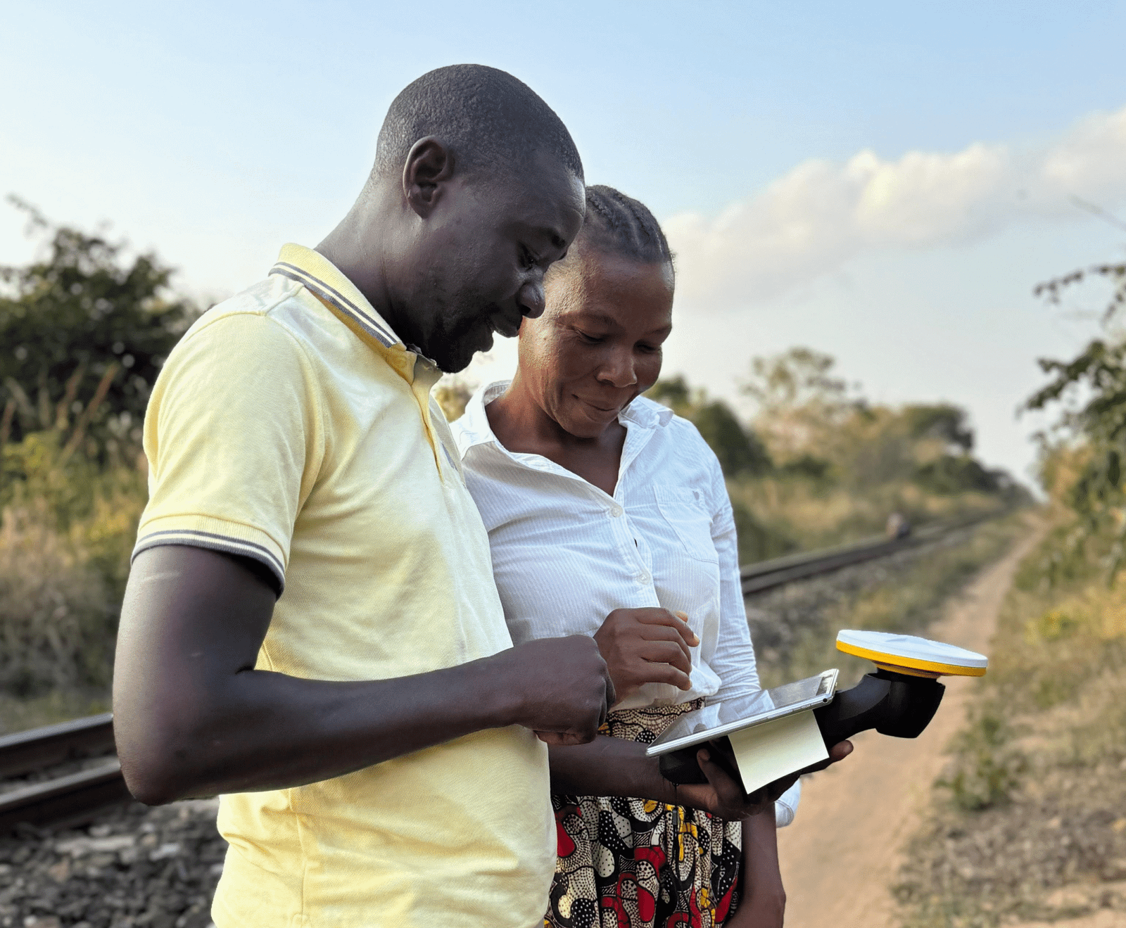 Two People Using a GpS Mapping Device near a Railway Track.